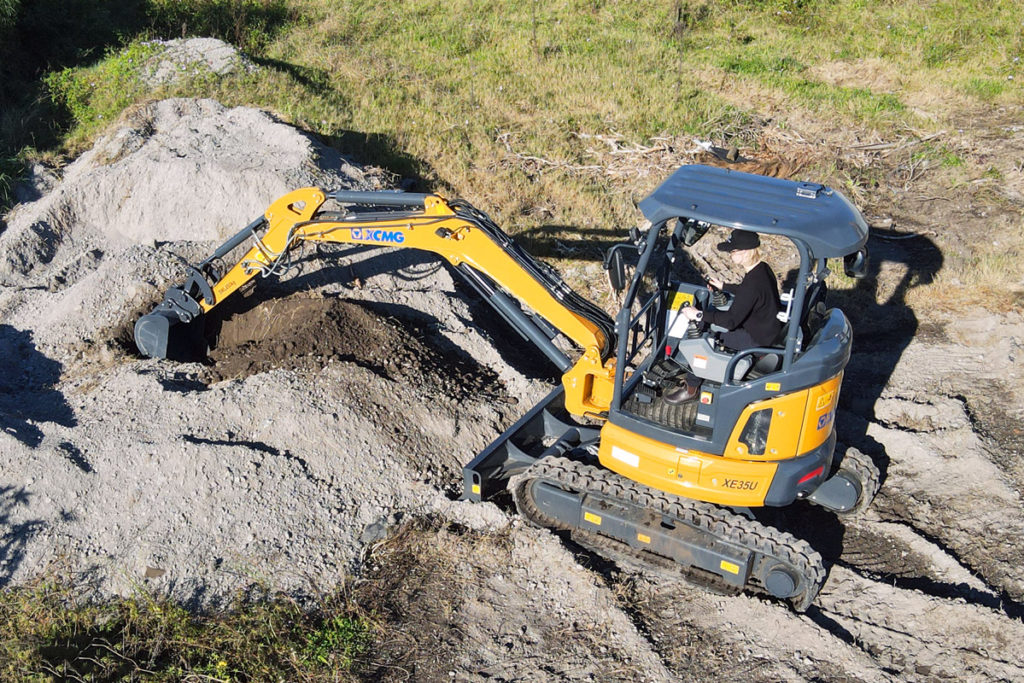 Mini excavator with operator digging a hole in sandy ground