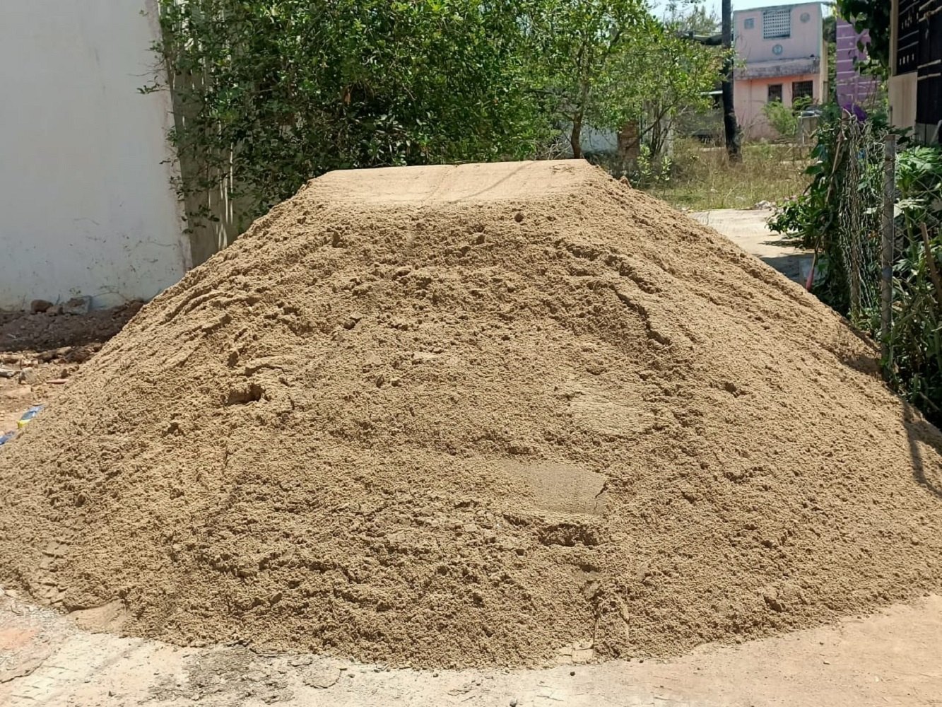 Pile of sand in a yard beside a wall and garden