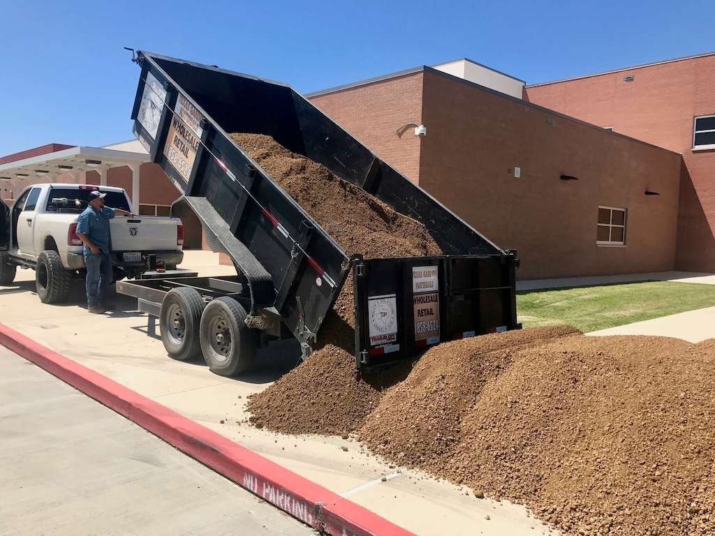 Tipper trailer behind a pickup dumping a load of soil on a driveway